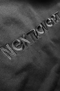 Close-up of the 'Nextrovert' logo embroidered in black on fabric, highlighting the texture and stitching detail.